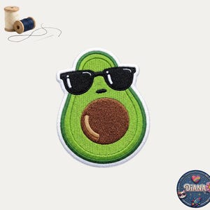 May include: An embroidered patch shaped like an avocado wearing black sunglasses, featuring a light green center, a dark brown pit, and a white border. Included are two wooden spools of thread, one beige and one dark blue, with a needle and thread.