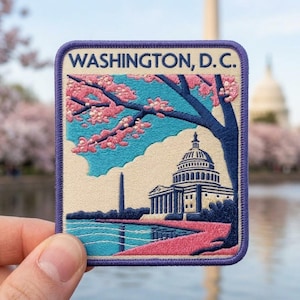 May include: A rectangular embroidered patch with a purple border featuring the text WASHINGTON, D.C. at the top. The design depicts the U.S. Capitol building, the Washington Monument, and a cherry blossom tree with pink flowers against a blue sky.