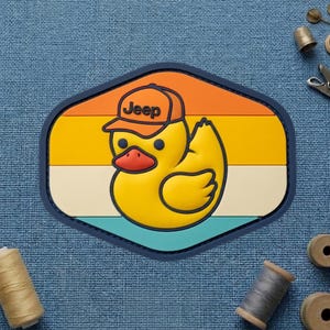 May include: A yellow rubber duck wearing an orange and brown Jeep hat, set against a retro sunset design. The patch has a navy blue border and is shaped like a hexagon. The word "Jeep" is printed on the hat.