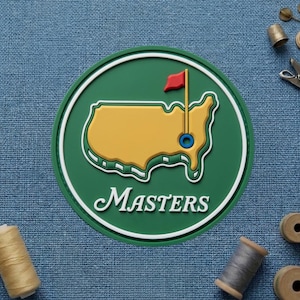 May include: A green and white circular emblem featuring a yellow outline of a map with a red flag and the word "Masters" in white script. The emblem is on a blue textured surface.
