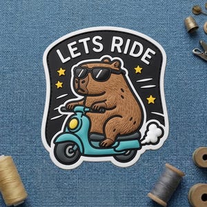 May include: A patch featuring a brown capybara wearing sunglasses and riding a teal scooter. The patch has the words "LETS RIDE" in white on a black background, with yellow stars and white accents.