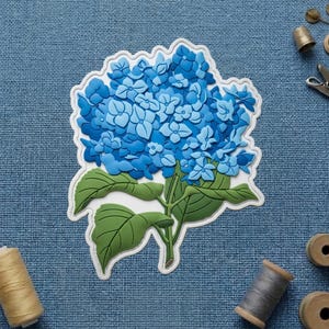May include: A blue hydrangea flower with green leaves and a white border. The flower is a mix of light and dark blue shades. The image is on a blue textured background.
