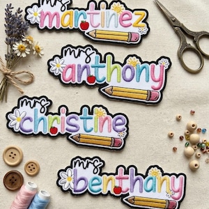 May include: Four embroidered name patches featuring the text mrs martinez, mrs anthony, mrs christine, and mrs benthany. Each patch includes a white daisy, a red apple, a yellow sun, and a yellow pencil with a pink eraser on a white background.