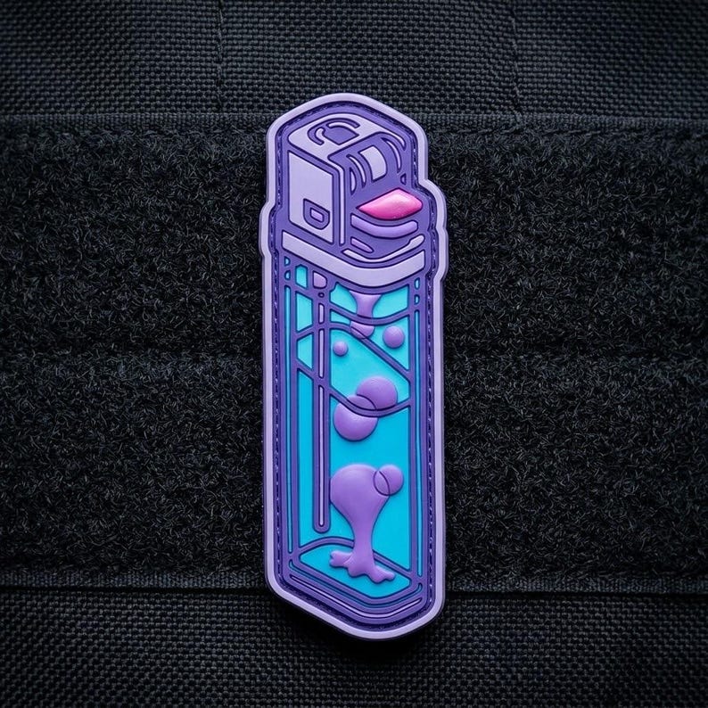 May include: A purple and blue patch in the shape of a lighter with a lava lamp design. The lighter has a purple outline, a blue body, and purple lava-like shapes inside. The background is black.