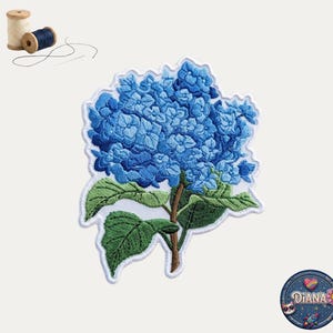 May include: Embroidered patch featuring a vibrant blue hydrangea flower with green leaves and a brown stem. The patch has a white border. A spool of thread and a needle are in the upper left corner. A circular patch with the name "DIANA" is in the lower right corner.