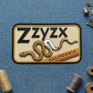 May include: A rectangular patch with the word "Zzyzx" in black letters above a gold and white snake design. The word "CALIFORNIA" is at the bottom, with a brown and orange stripe design. The patch has a black border.