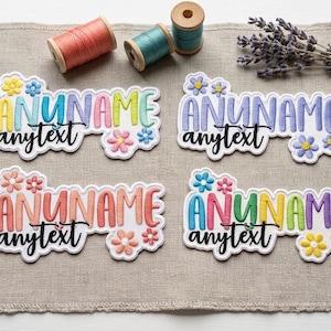 May include: Four embroidered patches with white backgrounds, each featuring the text ANUNAME in block letters and anytext in script, decorated with small flowers. The patches are surrounded by sewing supplies including thread spools, buttons, and scissors.