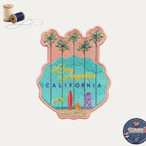 May include: An embroidered patch featuring a beach scene with palm trees, a red surfboard, a sandcastle, and a lifeguard tower. The text reads Los Angeles CALIFORNIA in yellow and blue. Two spools of thread and a needle are visible nearby.