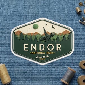 May include: A green, white, and tan Endor National Park patch with a landscape design featuring a crashed spaceship, trees, and mountains. The text "ENDOR" and "Home of the Ewoks" are displayed.