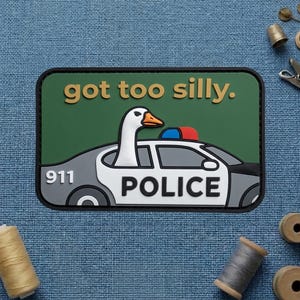 May include: A rectangular patch featuring a cartoon goose in a police car. The patch has a green background with the text "got too silly." The police car is gray and white with the word "POLICE" and the number "911."