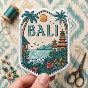 May include: An embroidered patch featuring a tropical landscape with the word BALI in teal letters. The design includes palm trees, a pagoda, mountains, a sun, and ocean waves in shades of teal, green, orange, and cream, with a white border.