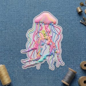 May include: A colorful jellyfish-shaped patch with a white border. The jellyfish has a pink and yellow dome, with long, flowing tentacles in shades of pink, blue, green, and yellow. The patch is on a blue fabric background.