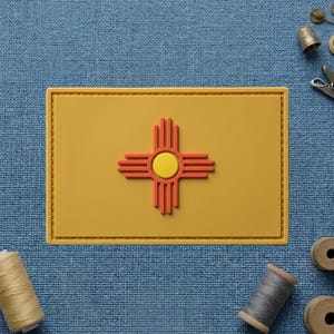 May include: A rectangular patch featuring the New Mexico state flag design. The patch has a yellow background with a red and yellow Zia sun symbol in the center. The patch is surrounded by a yellow border.