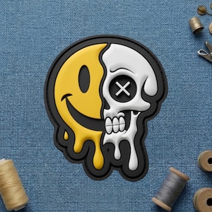 May include: A black-bordered patch featuring a split design: a yellow smiley face melting into a white skull. The skull has an X for an eye and dripping details. The patch is on a blue fabric background.