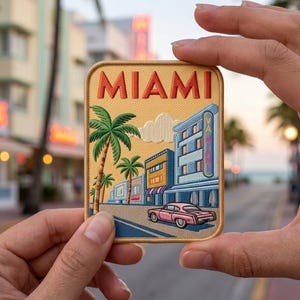 May include: A rectangular embroidered patch featuring a yellow background with the word MIAMI in orange letters. The design depicts a street scene with palm trees, blue buildings, a pink vintage car, and a vertical sign reading MIAMI.