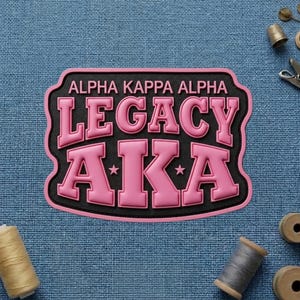 May include: A pink and black patch with the text "ALPHA KAPPA ALPHA LEGACY AKA". The patch has a black border and pink lettering. Two small stars are on the patch.