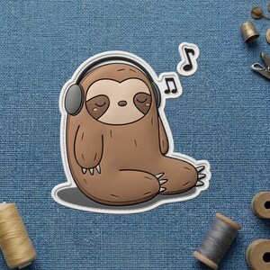 May include: A brown sloth sticker with a gray outline, wearing gray headphones and listening to music. The sloth is sitting with its eyes closed, and musical notes are floating above its head. The sticker is on a blue denim background.