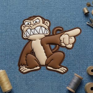 May include: A brown and tan cartoon monkey with an angry expression, pointing its finger. The monkey has a wide grin showing its teeth. The image is on a blue textured background.
