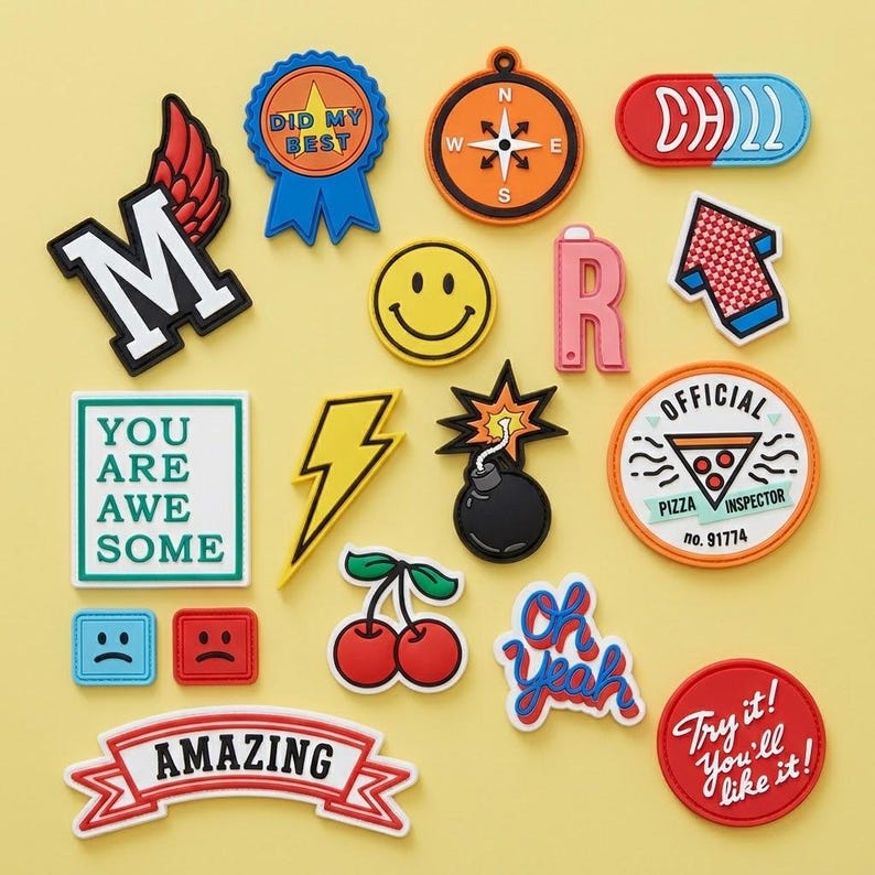 May include: A collection of colorful, decorative patches with various designs and text. Includes a lightning bolt, a smiley face, a compass, a pizza inspector badge, and patches with the words "AMAZING", "YOU ARE AWESOME", and "Try it! You'll like it!"