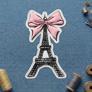 May include: A pink bow tops a black and white Eiffel Tower design. The tower is outlined in black and has a white border. The image is on a blue textured background.