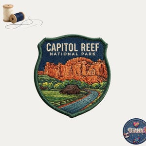 May include: A shield-shaped embroidered patch featuring the text CAPITOL REEF NATIONAL PARK in white. The design depicts orange rock formations, a green field, a brown cabin, and a blue river. Two spools of thread and a needle are nearby.