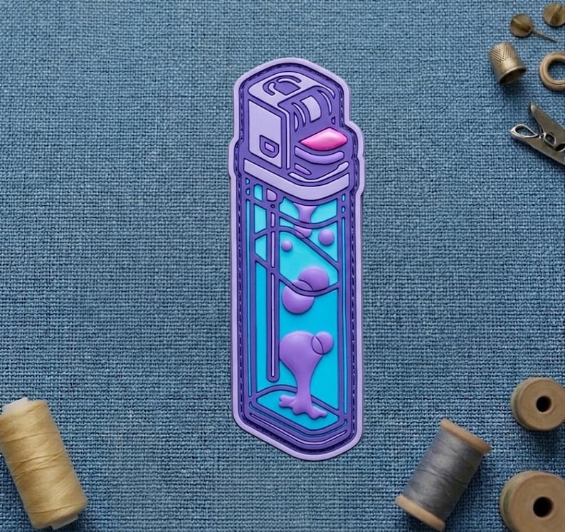 May include: A purple and blue sticker in the shape of a lighter, featuring a lava lamp design. The sticker has a purple outline, a light blue interior, and purple lava-like shapes inside. The top of the lighter is a lighter shade of purple with a pink detail.