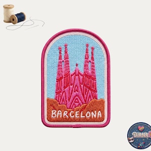 May include: An embroidered patch featuring the Sagrada Familia in pink against a light blue sky, with a brown base and the text BARCELONA in white. The patch has a pink border and is accompanied by two small spools of thread and a needle.