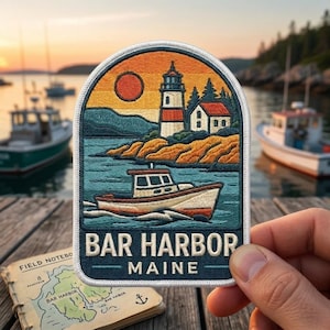 May include: An embroidered patch with a white border featuring a coastal scene of a lighthouse, a small boat on water, and a sunset. The text reads BAR HARBOR MAINE in white capital letters. The design includes orange, blue, and white thread colors.