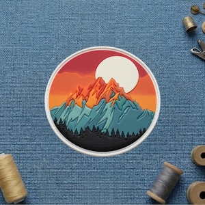 May include: A circular embroidered patch featuring a landscape design with a large white sun, orange and red sky, jagged mountain peaks in shades of orange and blue, and a dark silhouette of a forest at the base, all enclosed in a white border.