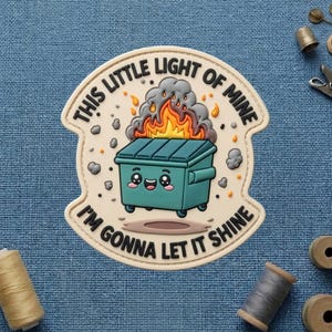 May include: A patch with the text "THIS LITTLE LIGHT OF MINE I'M GONNA LET IT SHINE" surrounds a teal dumpster on fire. The dumpster has a smiling face. The patch is beige with a stitched border.