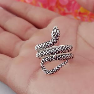 以下が含まれることがあります： 銀色のヘビの指輪、コイル状のデザイン。 指輪は、詳細なヘビの頭と体、質感のある鱗が特徴です。 この指輪はジュエリーです。