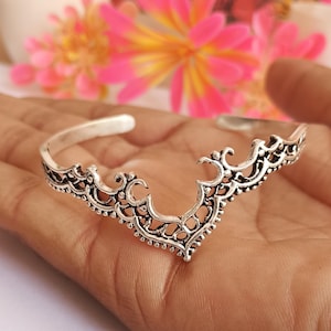 May include: Silver open cuff bracelet with an ornate, filigree design. The bracelet features a central V-shape with intricate patterns and openwork details. The bracelet is approximately 15 cm in circumference.