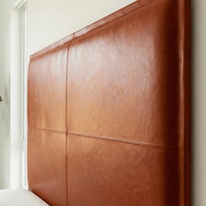 Puede incluir: Cabecero rectangular grande tapizado en cuero liso color caramelo. El cabecero está dividido en cuatro secciones por costuras, lo que añade un sutil patrón geométrico. El cuero tiene un ligero brillo.