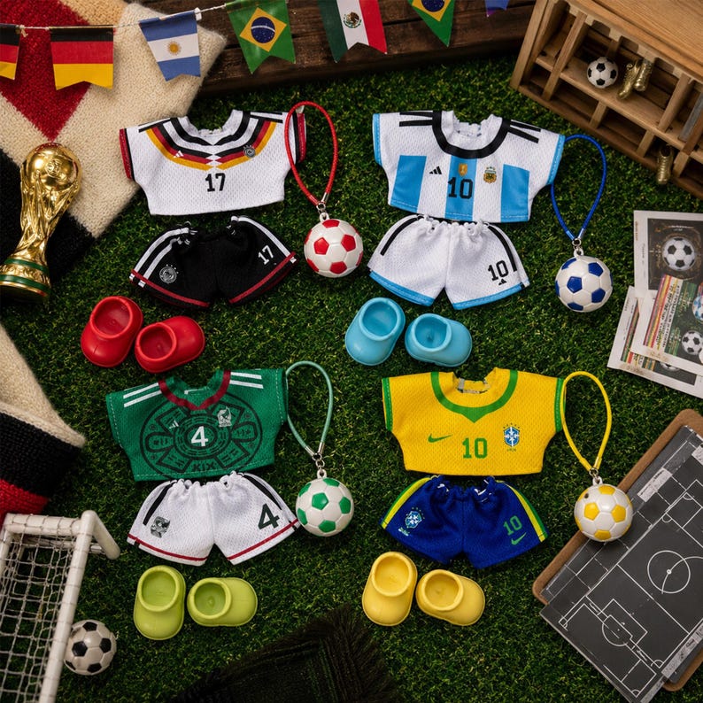 May include: Four sets of doll-sized soccer uniforms including jerseys, shorts, and shoes, featuring the national team colors and logos of Germany, Argentina, Mexico, and Brazil, accompanied by four miniature soccer ball keychains.