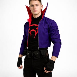 May include: A purple cropped jacket with a red collar and lining, worn over a black shirt with a red graphic. The outfit includes black gloves and a utility belt with pouches. The jacket has a zipper closure.