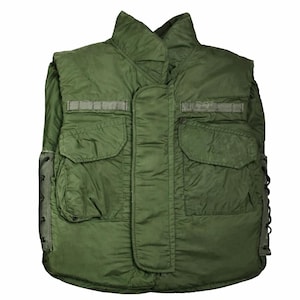 May include: An olive green military-style vest with a high collar and multiple pockets. The vest has a quilted design and reinforced shoulder areas. It features two large front pockets and smaller pockets above them. The sides have adjustable lacing.
