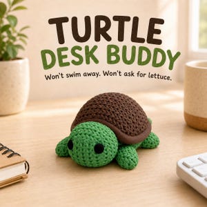 May include: A small, crocheted turtle figurine with a bright green head and limbs and a dark brown textured shell. The text above the turtle reads: TURTLE DESK BUDDY. Won't swim away. Won't ask for lettuce. The turtle has two round black eyes.