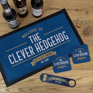 May include: A blue doormat, coasters, and bottle opener set with the text "WELCOME TO THE CLEVER HEDGEHOG" and "LET'S GET DRUNK EST. 2022". A bottle opener reads "THE SMITH'S PUB EST. 2021".