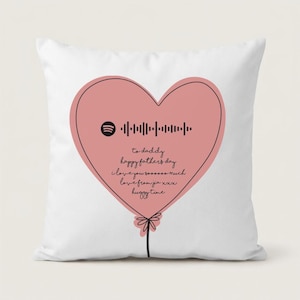 May include: A white throw pillow featuring a large pink heart-shaped design. The heart contains a Spotify code and text that reads "to daddy, happy father's day, I love you soooooo much, love from jia xxx, huggy time."