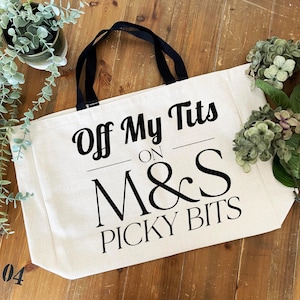 May include: A cream-coloured canvas tote bag with black handles and black printed text that reads Off My Tits ON M&S PICKY BITS. The bag features a rectangular shape with a flat bottom and is constructed from a woven fabric material.