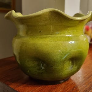 May include: A lime green ceramic bowl with a ruffled, wavy rim and a visible crackle glaze finish. The body of the bowl features subtle, rounded indentations around its circumference, creating a textured appearance on the glossy surface.