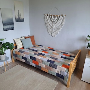 Puede incluir: Una cama de madera con una colcha de retazos colorida en tonos azules, naranjas y beige. Cojines decorativos de varios colores descansan sobre la cama. Un tapiz de macramé y obras de arte enmarcadas decoran la habitación.