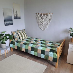 Peut inclure: Un lit simple avec une courtepointe patchwork aux carrés verts, bleus et beiges. Deux oreillers décoratifs avec des motifs géométriques et rayés. Une tenture murale en macramé et des œuvres d'art encadrées ornent la pièce.
