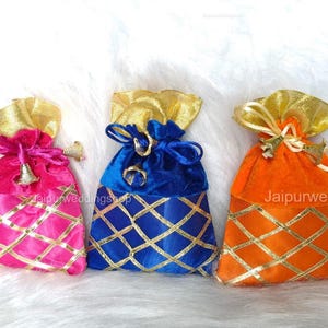 May include: Three colorful velvet drawstring bags. The bags are pink, blue, and orange, with gold accents. Each bag has a gold top and a gold lattice pattern on the bottom. The bags are tied with a matching drawstring.