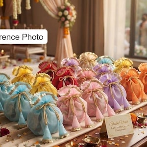 Op de afbeelding: Een verzameling kleine, semi-transparante buideltjes met trekkoord in diverse pastel- en felle kleuren, waaronder lichtblauw, geel, rood, roze, paars en oranje. Elk buideltje heeft een gouden trekkoord met kwastjes en een decoratieve rand.