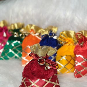 May include: A collection of colorful velvet pouches with gold accents. The pouches are in various colors, including red, orange, green, and blue. Each pouch has a gold drawstring and a gold diamond pattern.