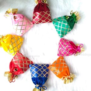 May include: A collection of eight colorful velvet gift bags arranged in a circle. Each bag is a different color, including red, pink, yellow, green, blue, and orange, with a gold lattice pattern and gold ribbon ties.