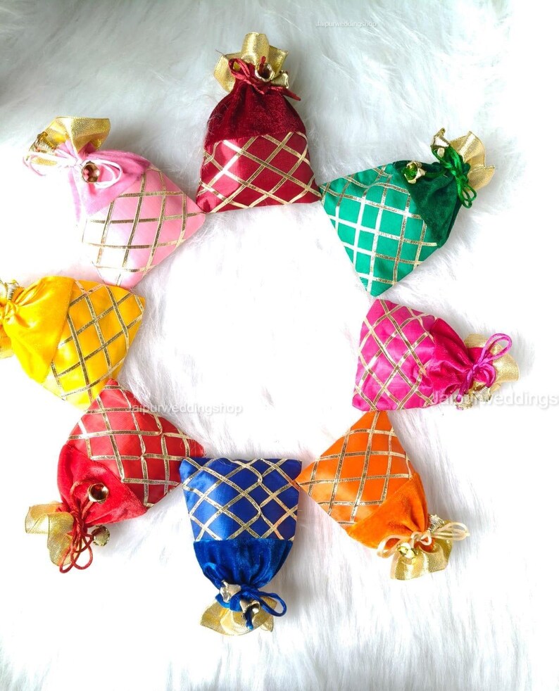 May include: A collection of eight colorful velvet gift bags arranged in a circle. Each bag is a different color, including red, pink, yellow, green, blue, and orange, with a gold lattice pattern and gold ribbon ties.