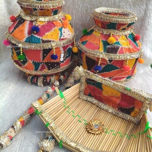 May include: Two round pots and a rectangular tray made of bamboo sticks, all decorated with multicoloured patchwork fabric, gold metallic fringe trim, and small pom-poms. The text Jaipurweddingshop is visible on the items in the image.