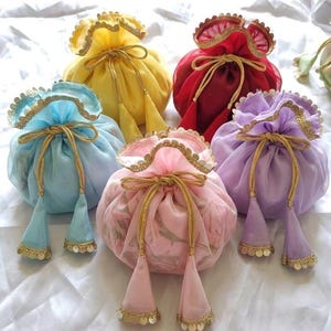 Peut inclure: Plusieurs pochettes décoratives à cordon colorées. Les pochettes sont de couleurs jaune, rouge, bleu, rose et violet. Chaque pochette a une bordure et un cordon dorés, avec des glands assortis ornés de sequins dorés.